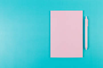 Top view of pink notebook, pink pen on blue background. School, office wallpaper. Flat lay, copy space.