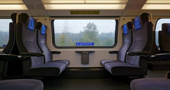 Empty first class bench seats inside moving public passenger train in Europe. Wide angle view, large windows, rainy autumn, green field nature background real time, no people