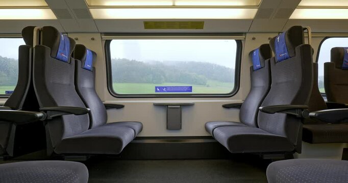 Empty first class bench seats inside moving public passenger train in Europe. Wide angle view, large windows, rainy autumn, green field nature background real time, no people
