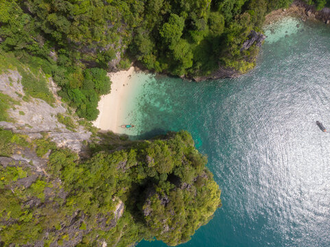 Aerial view of a secluded tropical beach surrounded by lush greenery and clear blue waters.
