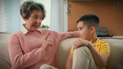 Caucasian grandmother explaining punishing spoiled grandson strict shaking index finger elderly...