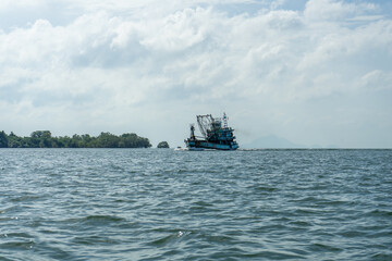 A fishing boat sails across a calm sea under a cloudy sky.