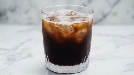 Cold brew coffee in a clear glass, condensation on the outside, on white marble background.