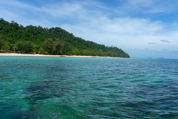 A serene view of a tropical beach with clear blue waters and lush green hills.