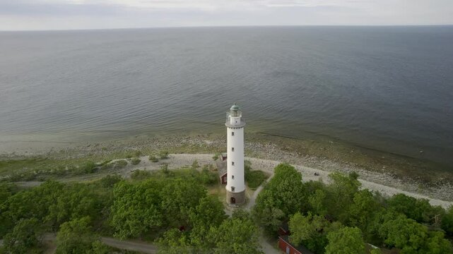 Aerial view of the beautiful lighthouse Lange Erik by the serene coastline with lush trees and calm sea, Oland Island, Sweden.