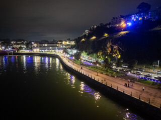 Fototapeta premium Tourists walking on illuminated promenade by the sea at night