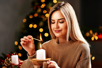Eine Frau zündet zu Weihnachten mit einem Streichholz eine Kerze an
