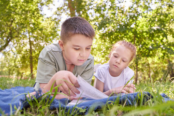 Fototapeta premium Children reading together in a sunny park: summertime learning and friendship in a green outdoor setting.