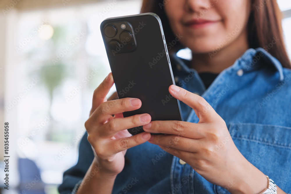 Wall mural Closeup image of a woman holding and using mobile phone in cafe