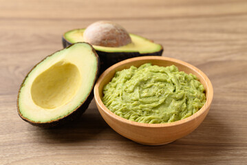 Mashed avocado in wooden bowl and Hass avocado fruit on wooden background, Healthy eating