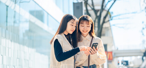 街中でスマホを見る友達同士の若い女性