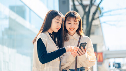 街中でスマホを見る友達同士の若い女性