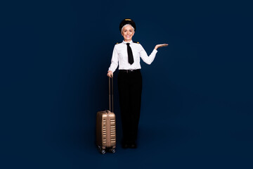 Full size photo of retired female airline pilot suitcase hold empty space wear aviator uniform isolated on dark blue color background