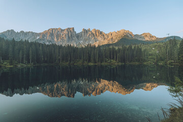 View of Lago di Carezza with tranquil reflections surrounded by majestic mountains and serene forest, Nova Levante, Italy.