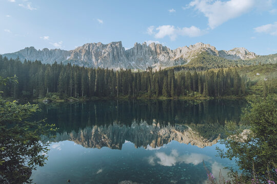 View of Lago di Carezza with tranquil reflection of majestic mountains and forest, Nova Levante, Italy.