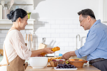 A woman prepares fresh vegetables in a cozy kitchen, while a man assists in the background. The scene emphasizes a warm and healthy lifestyle with a focus on fresh produce and home cooking.
