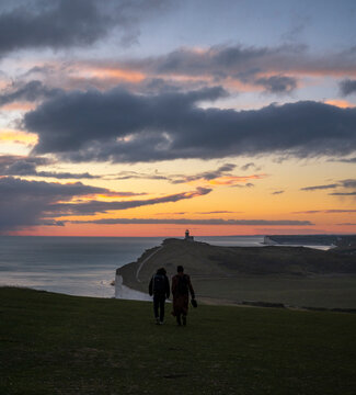 View of belle tout lighthouse at sunset with a couple on the cliff, seven sisters cliffs, eastbourne, east sussex, united kingdom.