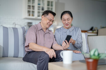 An elderly couple sits together in their cozy living room, smiling and enjoying a moment as they look at something on a smartphone. Their warmth and affection capture a peaceful home atmosphere.