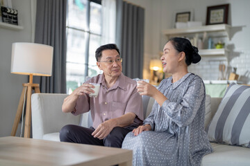 An elderly couple enjoys a peaceful moment at home, sharing smiles and drinks. The warm and cozy atmosphere emphasizes their deep connection, happiness, and the comfort of spending time together.