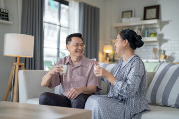 An elderly couple enjoys a peaceful moment at home, sharing smiles and drinks. The warm and cozy atmosphere emphasizes their deep connection, happiness, and the comfort of spending time together.
