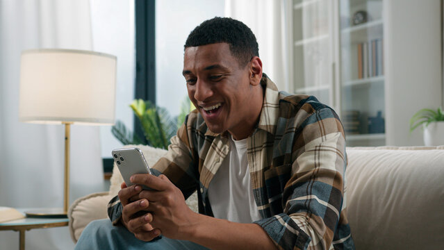 Surprised excited African American shocked man winner win smartphone achieve read good internet news amazed by mobile phone achievement winning victory success online bet bid game happy guy at home
