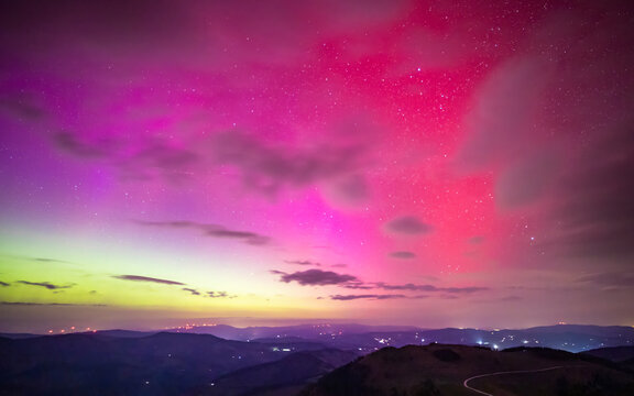 View of aurora borealis illuminating a colorful night sky over serene mountains and clouds, Almenland, Austria.