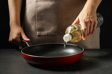 Woman pouring oil into frying pan at dark gray textured table, closeup