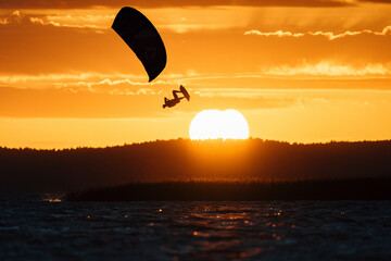 Extreme kitesurfing move of kiteboarder jumping high in the epic sunset sky.