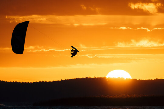 Extreme kitesurfing move of kiteboarder jumping high in the epic sunset sky.