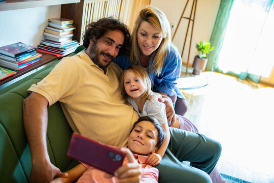 Happy family taking group selfie on couch at home - Powered by Adobe