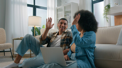 African American couple on floor at home using online laptop computer browsing shopping together...