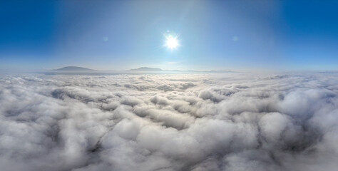 A serene view of the early morning sun rising above a vast sea of clouds, with distant mountain peaks faintly visible on the horizon, creating a peaceful and ethereal landscape. Flying over the cloud