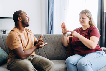 Happy young woman and man using sign language, sitting on couch at home