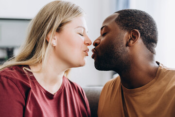 Loving multiethnic couple kissing sitting on sofa at home