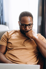 Focused young African American man working with laptop sitting at home