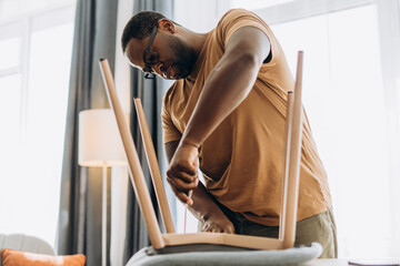 African American young man fixing a chair with a screwdriver at home
