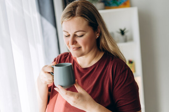 Caucasian pretty woman looking at cup of coffee posing at home at home