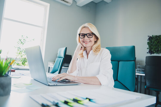 Photo of project manager it development blonde hair smiling senior woman sitting on workplace with netbook having qa session