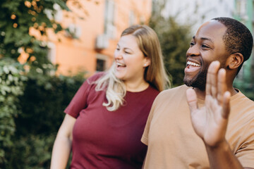 Happy multiracial couple walking outdoors, African American man waving his hands