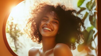 A woman with curly dark hair smiles brightly, her eyes closed, as she looks towards the sun. Her face is glowing, and she appears to be happy and carefree.
