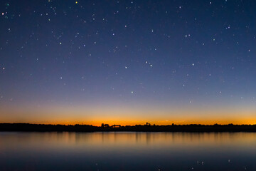 Sunset over river with stars in nature. Landscape sky concept. Dark night with stars and a wide river with forest in the evening. The river flowing through the forest in the evening with stars dark.