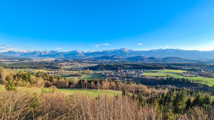 Naklejka premium Panoramic view of majestic mountain range Karawanks and Kamnik-Savinja seen from Sternberg in Wernberg, Carinthia, Austria. Valley covered by idyllic forest in Austrian Alps. Tranquil alpine landscape