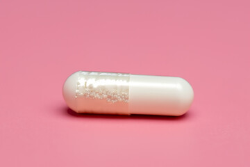 Capsule in pink and white on white. health medicine pill concept. small white capsule lying on a pale pink. a small white capsule lies on a pale pink with a blue and medical lifestyle terminology.