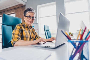Photo of nice retired woman working netbook wear plaid yellow shirt comfortable modern office room...