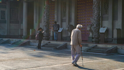 An elderly guy is walking alone with cane in the Chinese temple, Taipei, Taiwan in the summer. The...