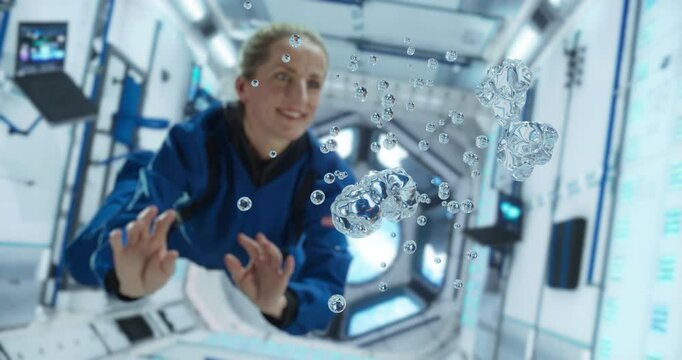 Female Cosmonaut in Blue Suit Interacts With Floating Water Droplets Inside a Space Station. Portrait of a Courageous Female Astronaut. Space Travel, Solar System Exploration and Colonization Concept