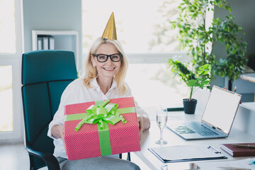 Photo of smiling businesswoman wearing white shirt birthday hat cone celebrate holiday at office...