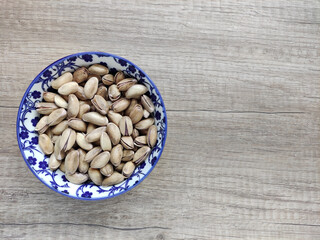 Fresh natural dried pistachios in a decorative plate on a wooden background