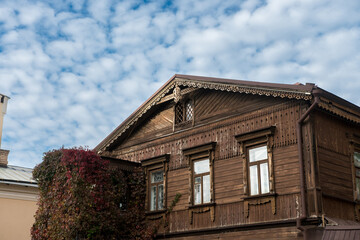 Old wooden house with ornate woodwork and autumn ivy, set against a backdrop of fluffy clouds. Ideal for architectural heritage, cultural tourism, or autumnal themes