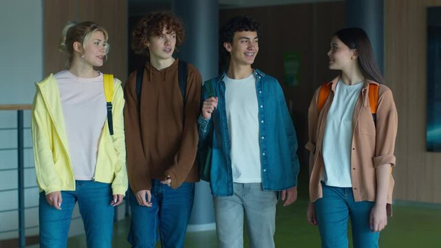 Four Caucasian students pupils men women girls guys boys female male teenagers teens friends walking going in school college university corridor talking friendly smiling communicate studying education